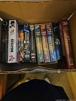 Box of assorted VHS tapes showing spines of multiple titles