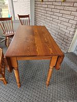 Full view of table showing drop leaf folded down, turned legs, wood grain