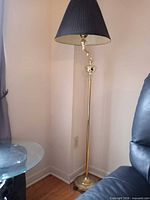 Full view of brass floor lamp in corner with black shade