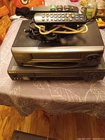 Stacked Sony and Citizen VCRs with cables and remote on top