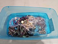Overview of assorted jewelry in blue plastic bin