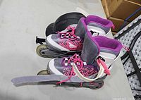 Pair of gray/pink kids inline skates side view with helmet partially visible