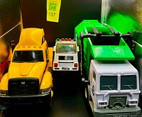 Front view of three toy trucks: yellow CAT semi, white utility truck, green garbage truck