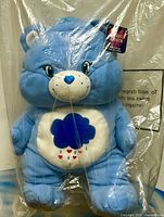 Front view of blue Care Bears plush inside protective bag with hang tag visible
