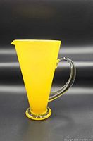Full front view of yellow glass pitcher, clear handle visible