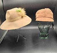 Both tan hats displayed on glass heads, felt hat left, suede cap right