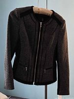 Front view of tweed jacket on hanger showing full zipper, pockets, trim