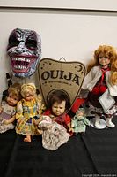 Group shot of five dolls, Ouija planchette, horror mask on stand