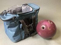Maroon bowling ball beside open blue bowling bag
