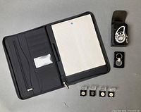 Open portfolio showing interior slots and notepad; clip watch, keychain and five boxed pins positioned alongside