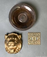 Group view of lion head plaque, metal bowl, ornate switch plate