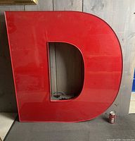 Front view of large red letter D sign with wiring visible inside; soda can for scale