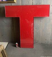 Large glossy red letter T leaning against wall with wire visible