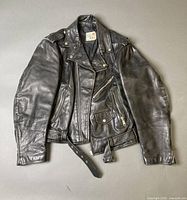 Front of black leather motorcycle jacket showing zipper, pockets, belt, epaulettes