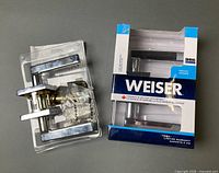 Two Weiser privacy lever handle sets, one sealed in retail box and one out of box but secured in blister tray with hardware