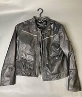 Front view of black leather motorcycle jacket showing overall design, chest and waist pockets, zipper and snaps