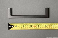 Single matte black metal drawer pull next to measuring tape showing 5.5 in length