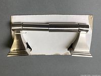 Front view of brushed nickel toilet paper holder on card backing showing both brackets and spring bar