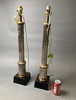 Pair of tall silver and gold accented column table lamps beside soda can for scale