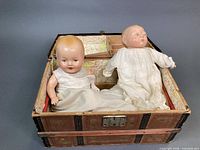 Trunk open showing two composition baby dolls seated inside on patterned interior