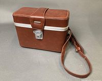 Closed brown leather case showing exterior, latch, strap