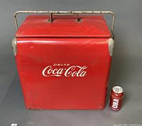 Front view of red Coca-Cola cooler beside soda can for scale
