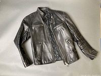 Front view of black leather motorcycle jacket showing zippers, pockets, collar, and quilted lining