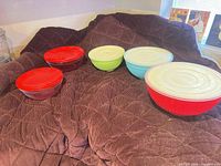 Five coloured and clear glass bowls with lids displayed on fabric