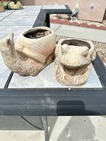 Frog and snail concrete planters side by side showing overall form and cavities