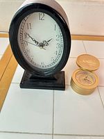 Black oval tabletop clock beside gold stacked-coin trinket box with built-in clock