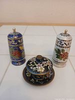 Pair of multicolour cloisonné salt and pepper shakers with gold finials, small cloisonné lidded bowl on matching saucer