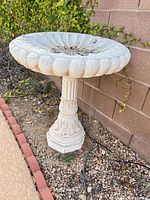 Full view of ornate concrete bird bath against wall