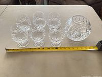 Six snifter glasses and matching bowl aligned beside measuring tape for scale