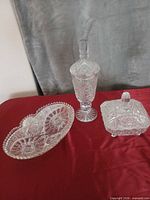 Three cut crystal pieces: tall covered urn, square lidded dish, oval divided dish displayed on red cloth