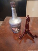 Silver metallic glass bottle with concert theme graphic beside brown wood display easel on table