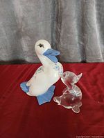 Porcelain duck and clear glass animal figurines on red cloth