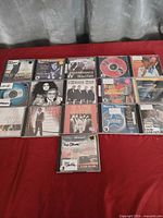 Group shot of all 16 CDs arranged on red surface showing covers and discs