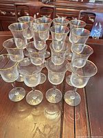 Front view of 16 clear glass wine glasses with gold rim arranged on wooden surface