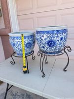 pair of blue and white porcelain planters on iron stands with measuring tape for scale
