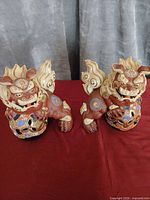 Both guardian lion figurines side by side on red surface