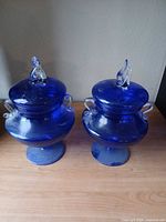 Front view of both cobalt blue lidded urn jars on tabletop