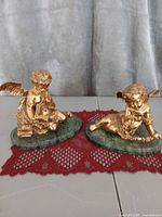 Both gilt cherub figurines on green marble bases displayed side by side