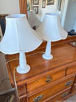 Two matching white ceramic table lamps with shades on dresser