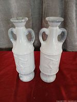 Front view of both white milk glass vases showing handles and relief athlete design
