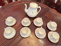 Entire tea set on table: teapot, four white cup-saucer sets, three pink floral cup-saucer sets (fourth not shown)