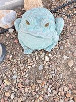 Front view of patina green resin frog statue on gravel