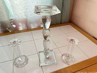 One tall faceted crystal candle holder flanked by two shorter glass candlesticks on tiled surface