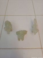Group view of the three pale green jade animal figurines on tile