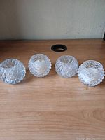 Four clear pressed glass tealight holders on tabletop showing size and diamond pattern