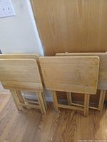 Four light wood folding TV tray tables leaning against wall